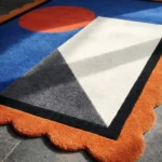 Close-up perspective of the Amber Solis rug highlighting the plush hand-tufted wool texture, the vibrant orange sun motif, and the decorative rust scalloped edge.