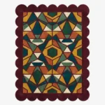 Top down view of the Autumn Prism rug featuring a complex geometric kaleidoscope pattern with faceted triangular shapes in rich autumn tones of ochre, rust, and forest green, finished with a deep burgundy scalloped border.