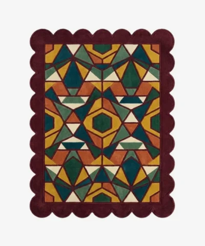Top down view of the Autumn Prism rug featuring a complex geometric kaleidoscope pattern with faceted triangular shapes in rich autumn tones of ochre, rust, and forest green, finished with a deep burgundy scalloped border.