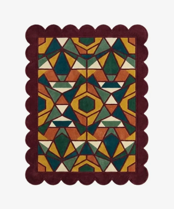 Top down view of the Autumn Prism rug featuring a complex geometric kaleidoscope pattern with faceted triangular shapes in rich autumn tones of ochre, rust, and forest green, finished with a deep burgundy scalloped border.