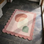 High angle view of the Blush Aurea rug featuring abstract organic shapes in rust, cream, and sage green, framed by a soft dusty rose scalloped border.