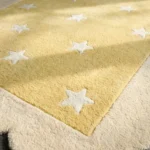 Close-up low angle view of the Buttercream Bloom rug, showcasing the plush hand-tufted wool texture, the embossed white star detail, and the intricately carved cream scalloped edge.