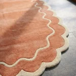 Close-up detail of the Cedar Patio rug's corner, showcasing the cream scalloped border and the thick, plush pile of the rust wool.