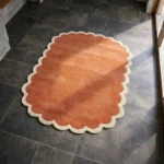 Perspective view of the Clay Veranda rug placed on a dark tiled floor, highlighting the warm clay tones and the plush hand-tufted wool texture.