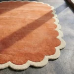 Close-up detail of the Clay Veranda rug, showcasing the soft cream scalloped edge and the dense pile of the rust-colored wool center.