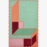 Top down view of the Coral Courtyard rug featuring an architectural geometric pattern with L-shaped blocks in fresh mint green and vibrant coral orange, finished with custom scalloped edges.