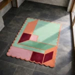 High angle view of the Coral Courtyard rug placed on a dark tiled floor, showcasing how the pastel mint and warm coral tones brighten up a modern living space.