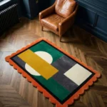 Angled view of the Dark Solis rug styled in a room with a leather chair, featuring a modern geometric design with a dark green field, yellow rectangular accent, and vibrant orange scalloped border.