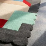 Close-up perspective of the Gentle Pulse rug, highlighting the plush hand-tufted wool texture and the vibrant contrast of the red and mint geometric shapes against the dark grey scalloped edge.