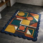 High angle view of the Harvest Loom rug featuring a bold geometric composition with mustard yellow, teal, and rust orange shapes, framed by a dark blue scalloped border.