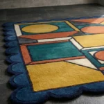 Close-up perspective view of the Harvest Loom rug, highlighting the thick hand-tufted wool texture and the vibrant contrast between the geometric blocks and blue border.