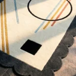Close-up perspective of the Incorix rug, showcasing the plush hand-tufted wool texture and the graphic contrast of the black circle and colorful lines against the cream pile.