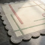 Close-up perspective of the Ivory Valette rug, highlighting the plush hand-tufted wool texture and the precise carving of the pastel geometric lines and scalloped edge.