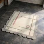 High angle view of the Ivory Valette Square rug featuring a minimalist geometric design with soft pink and green lines on a cream background, framed by a taupe scalloped border.