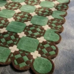 Close-up angled view of the Meadow Tiling rug, highlighting the plush hand-tufted New Zealand wool and viscose silk texture, the deeply carved lines defining the green squares, brown checkered patterns, and cream crosses, along with the intricately contoured scalloped edge.