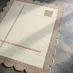 Close-up perspective of the Mist Alba rug, highlighting the plush hand-tufted wool texture and the precise carving of the beige scalloped edge and pastel geometric lines.