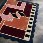 Close-up detail of the Muted Garnet rug, highlighting the plush hand-tufted wool texture and the architectural abstract pattern with a pink 3D-effect path and garnet color blocks.