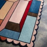Close-up detail of the Muted Studio Square rug, highlighting the plush hand-tufted wool texture and the architectural geometric pattern in contrasting muted tones of blue, rust, and red.