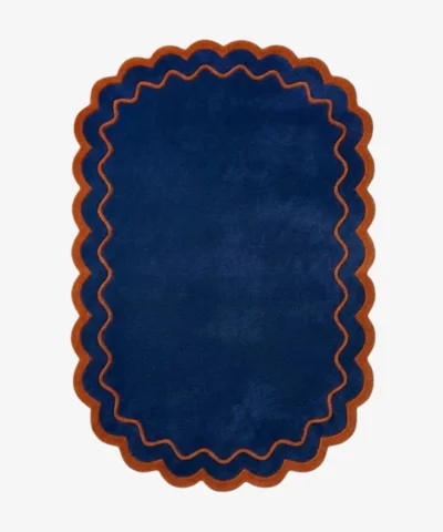 Top down view of the Ocean Garnet rug featuring a solid deep navy blue center framed by a rust orange wavy scalloped border.