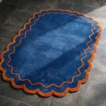 Close-up detail of the Ocean Garnet rug, showcasing the plush hand-tufted wool texture and the distinctive double wavy border in contrasting rust and blue.