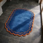 Perspective view of the Ocean Garnet rug placed on a dark tiled floor, highlighting the rich ocean blue tones and the warm garnet scalloped edge.