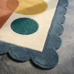 Close-up detail of the Ochre Loom rug highlighting the plush hand-tufted wool texture and the decorative blue scalloped edge next to a teal circle.