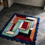 High angle view of the Offset Vault Square rug featuring a nested rectangular geometric design in burgundy, teal, and orange, framed by a dark blue scalloped border.