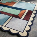Close-up detail of the Pastel Pocket rug's corner, showcasing the cream scalloped edge with dark blue binding and the thick wool pile.