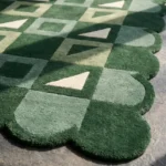 Close-up angled view of the Pine Patchwork rug, highlighting the plush, dense hand-tufted New Zealand wool and viscose silk texture, the deeply carved lines defining the interlocking green and cream geometric shapes, and the intricately contoured scalloped edge.