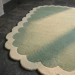 Close-up detail of the Pistachio Whale rug's corner, showcasing the cream scalloped edge and the thick wool pile fading from green to pastel tones.