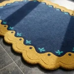 Close-up detail of the Royal Indigo rug's corner, showcasing the plush hand-tufted wool texture and the intricate teal leaf motifs on the gold scalloped edge.