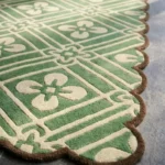 Close-up angled view of the Sage Dream rug, highlighting the dense hand-tufted New Zealand wool and viscose silk texture, the deeply carved lines defining the cream geometric lattice and floral motifs against the green, and the intricately contoured brown scalloped edge.