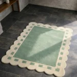 Perspective view of the Sage Frame rug placed on a dark tiled floor, highlighting the soft sage green tones and the elegant geometric border.