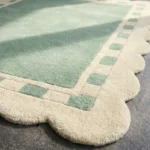 Close-up detail of the Sage Frame rug's corner, showcasing the plush hand-tufted wool pile, the cream scalloped edge, and the intricate square border design.
