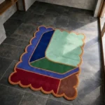 High angle view of the Soft Lagoon rug featuring a modern abstract geometric design with interlocking color blocks in mint green, deep blue, and burgundy, framed by a rust orange scalloped border.