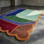 Perspective view of the Soft Lagoon rug highlighting the plush hand-tufted wool texture and the vibrant contrast of the rust scalloped edge against the cool green and blue geometric shapes.