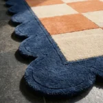 Close-up perspective of the Solace Tide rug, highlighting the plush hand-tufted wool texture and the contrasting blue scalloped edge against the rust check design.
