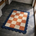 High angle view of the Solace Tide rug featuring a warm rust and cream checkerboard pattern, framed by a deep blue scalloped border.