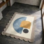 High angle view of the Still Shore rug placed on a dark tiled floor, showcasing the soft pastel colors and modern abstract shapes that create a serene atmosphere.