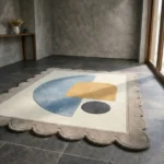 High angle view of the Still Shore rug placed on a dark tiled floor, showcasing the soft pastel colors and modern abstract shapes that create a serene atmosphere.