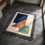 Perspective view of the Stone Leaf rug on a dark tiled floor, showing how the natural sunlight highlights the plush hand-tufted wool texture and the geometric color blocks.