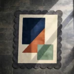 The Stone Leaf rug styled in a room with a leather armchair and dark blue walls, highlighting how the grey border and earthy geometric shapes complement mid-century modern furniture.