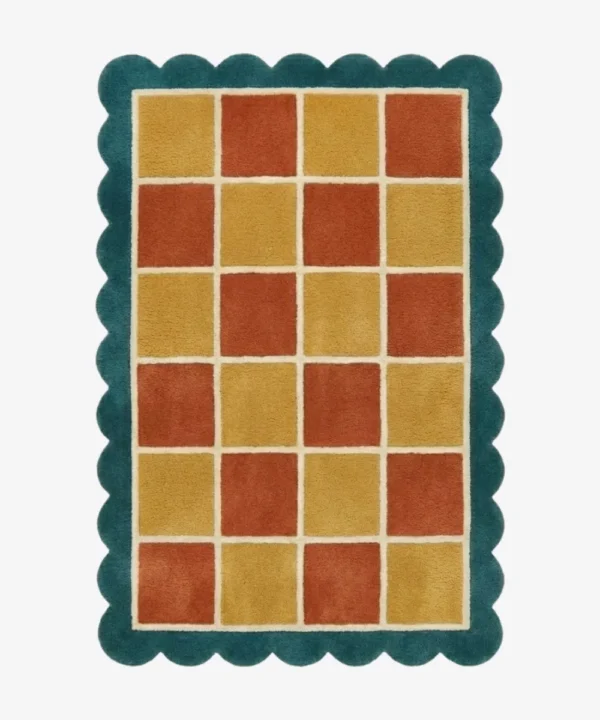 Top down view of the Sunbathe Quilt rug featuring a vibrant checkered pattern in rust orange, mustard yellow, and peach, framed by a cream line and a teal green scalloped border.