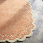 Close-up detail of the Terra Manor rug's border, showcasing the cream scalloped edge with intricate tufted dots and wavy line accents against the rust wool.