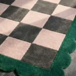 Close-up perspective of the Verda Current rug, highlighting the plush hand-tufted wool texture and the striking contrast of the emerald green scalloped edge against the pink and grey check design.