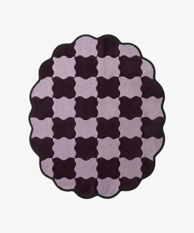 Top-down view of the round Amora Weave rug, featuring a whimsical wavy checkerboard pattern in alternating shades of light lilac and deep plum purple, framed by a continuous black scalloped border.