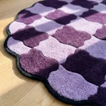 Close-up angled detail of the Amora Weave round rug in sunlight, highlighting the dense hand-tufted wool cut pile, the soft organic lines of the purple checkerboard pattern, and the crisp black scalloped binding.
