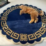 Perspective view of the circular Aurexion Loop rug styled on a light hardwood floor in a sunlit nursery, next to a white wooden crib with colorful canopies, featuring a cream field with a thick charcoal continuous loop pattern and scalloped border.