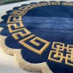 Close-up angled detail of the Aurexion Loop round rug, highlighting the thick, dense hand-tufted wool pile texture, the defined charcoal grey loop line, and the deeply carved charcoal scalloped border in natural light.