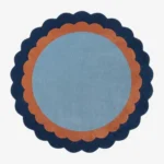 Top-down view of the circular Azure Halo rug featuring a light blue center framed by a double scalloped border in warm terracotta and deep navy blue.